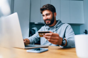 Cheerful young man paying bills thru online payment platforms