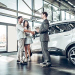 Young couple shaking hands with sales agent after a successful car loan application.