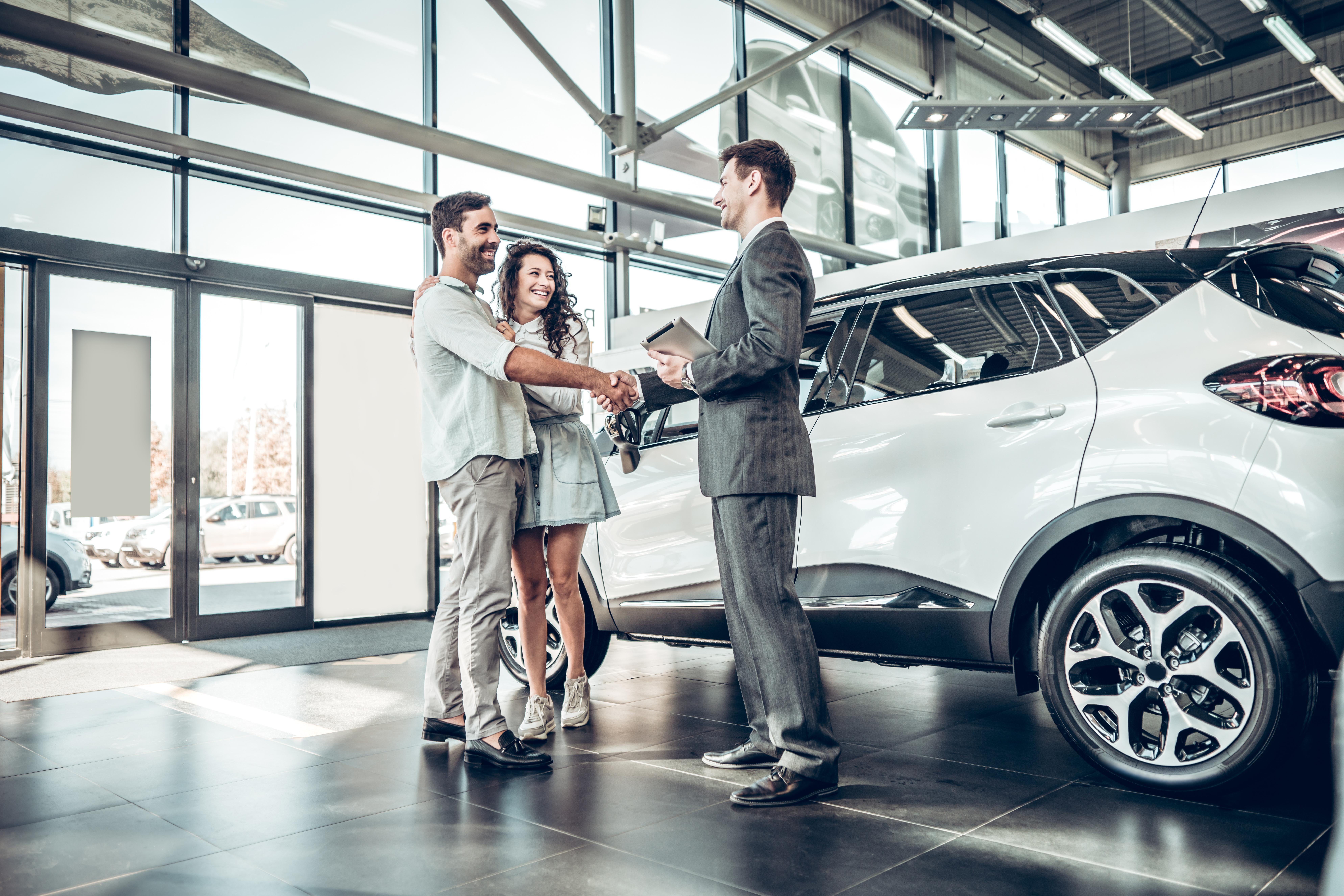 Young couple shaking hands with sales agent after a successful car loan application.