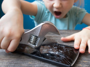 A little girl repairing a smartphone with a wrench