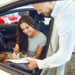 A young woman happily signing a car lease agreement