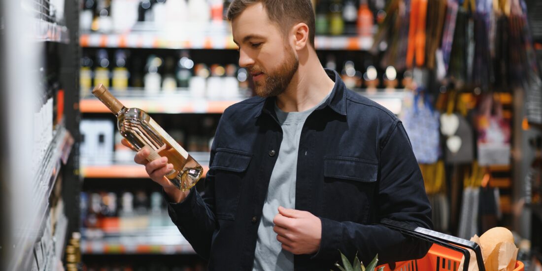 Man in a supermarket carefully reads wine label to avoid food fraud