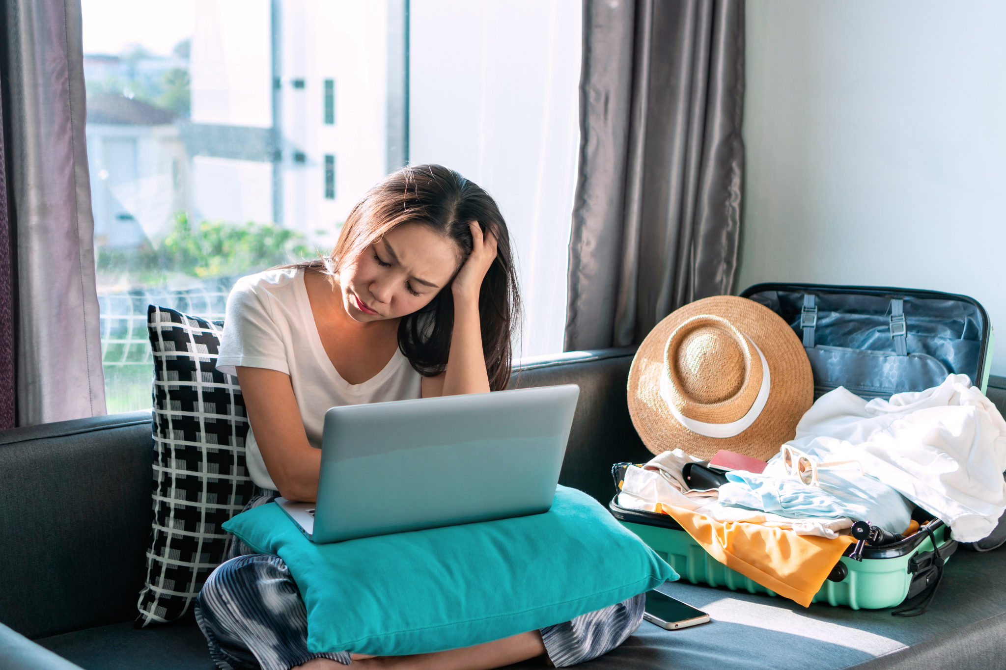 A woman feeling concerned about online booking scams while planning her summer vacation travel.