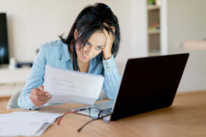 Frustrated woman looking at laptop while holding a rejected insurance claim