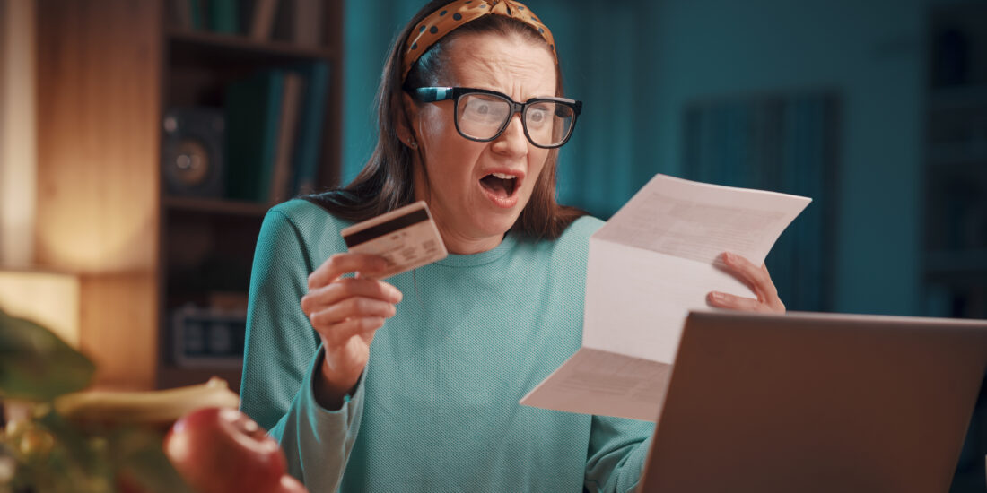 A shocked woman holding a credit card, staring at a paper bill in shock as she discovers excessive card surcharges