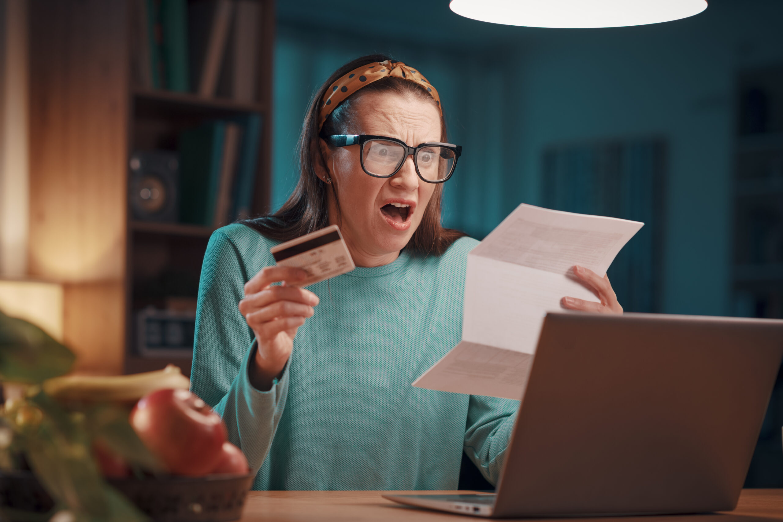 A shocked woman holding a credit card, staring at a paper bill in shock as she discovers excessive card surcharges