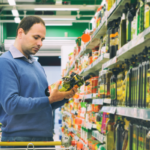 Man comparing products in a supermarket aisle, noticing price discrepancies