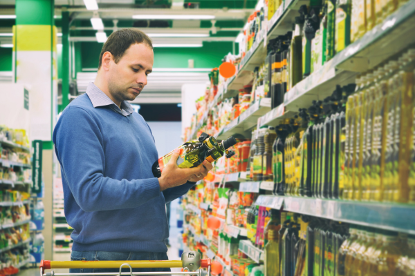 Man comparing products in a supermarket aisle, noticing price discrepancies