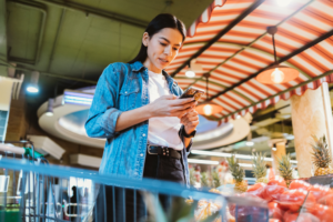 Woman using her phone in a supermarket to lodge a complaint about a pricing issue with Handle My Complaint