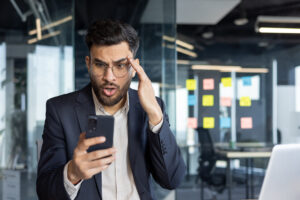 Frustrated businessman holding phone in office experiencing mobile service issues
