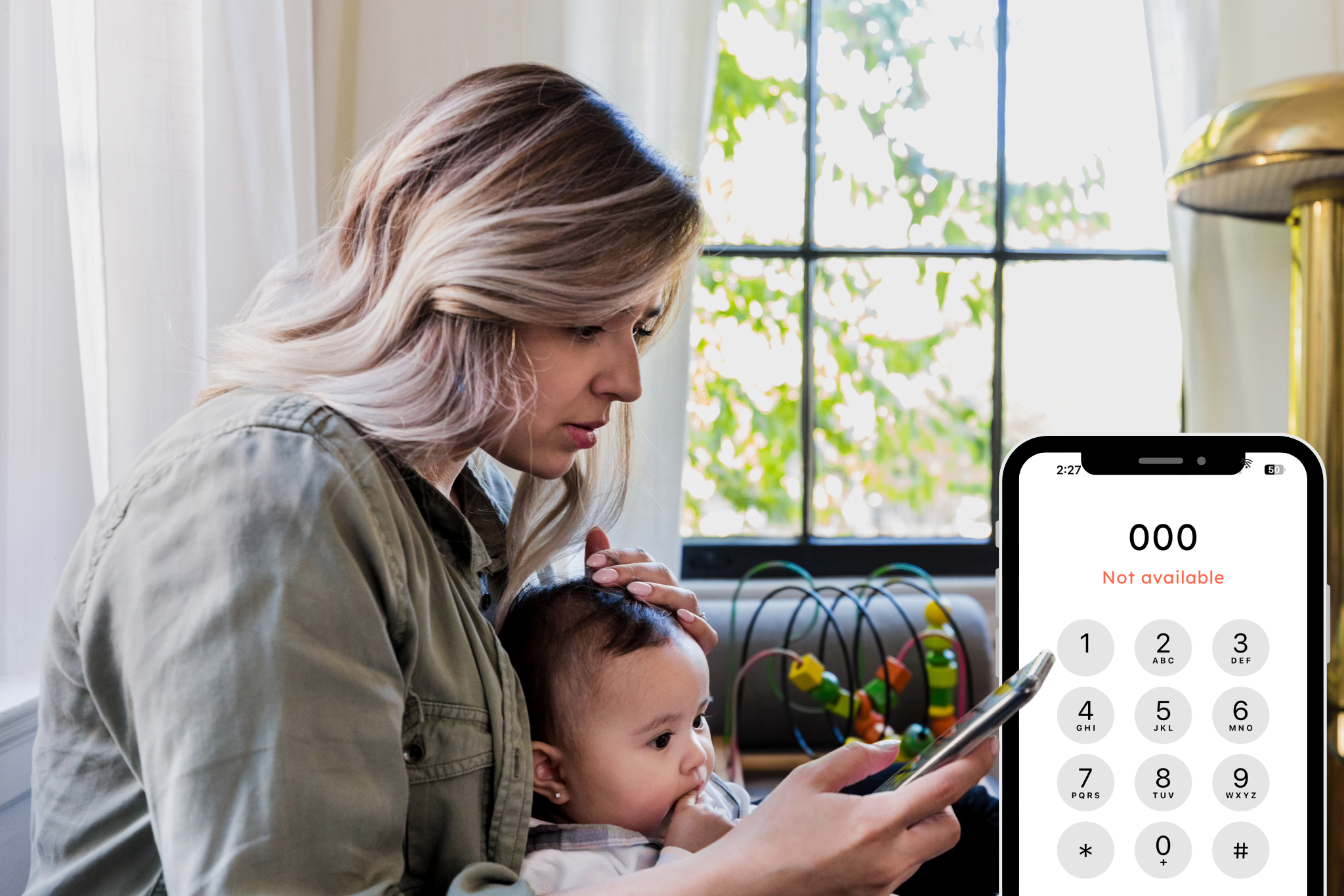 Worried woman holding baby, looking at phone displaying 'emergency call not available' message during telco outage
