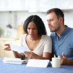 Frustrated couple reviewing unexpected transactions on a bank statement at home