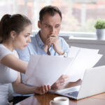 Frustrated couple at home reviewing bank statements and unpaid bills on a laptop, considering how to complain about a bank after a financial dispute