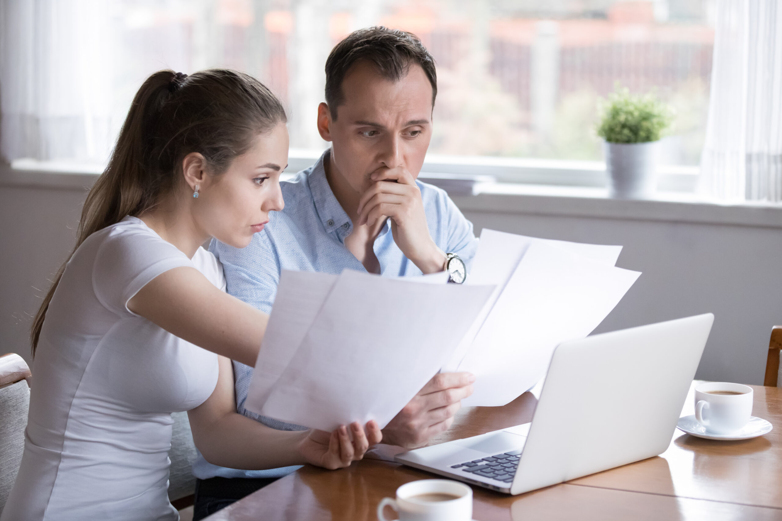 Frustrated couple at home reviewing bank statements and unpaid bills on a laptop, considering how to complain about a bank after a financial dispute