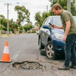 A man photographs a pothole beside his car, which has a flat tyre, as he gathers evidence for a potential damage claim